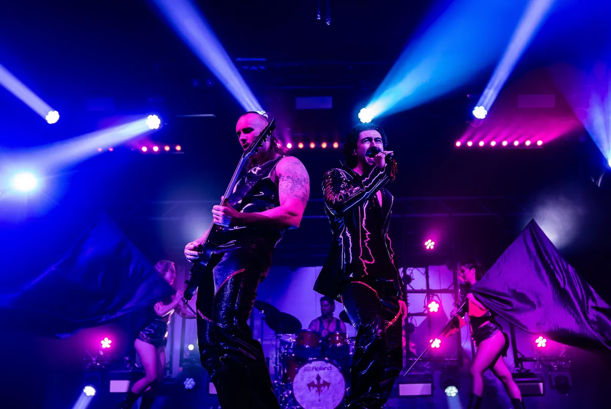A rock band and dancers on stage under blue spotlights during the Dracula's Gold Coast show